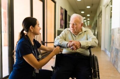 Which-Should-I-Choose-Nursing-home-Care-or-Hospice-Care-Young-nurse- kneeling-down-to-talk-with-an-older-man-in-wheelchair