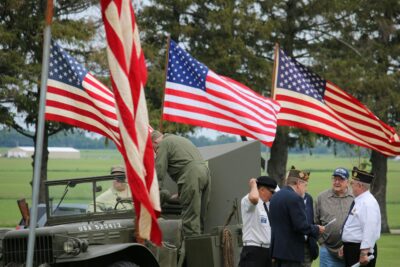 Group of elderly veterans standing with American Flags in a park.
