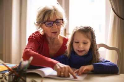 Grandmother helps her young granddaughter with her homework at the kitchen table.