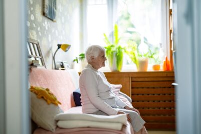 Senior woman sits alone on sofa staring ahead