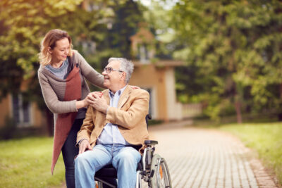 caregiver daughter pushing elderly father in his wheelchair outside.