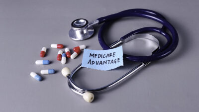 Medicare Advantage Concept with Stethoscope, Note, and Capsules on Gray Background