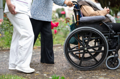Senior woman in wheel chair with relative and nurse caregiver, outdoors at nursing home garden.